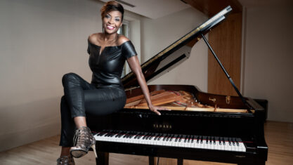 Jade Simmons posing on the side of a grand piano wearing a black dress