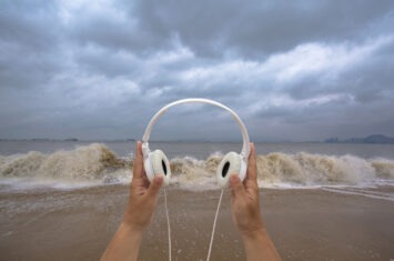 hand holding earphone on beach,listening to waves sounds