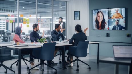 businesspeople in conference room talking woman on video conferencing screen