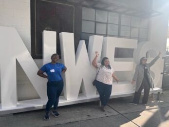 three women posing in front of letter sculpture