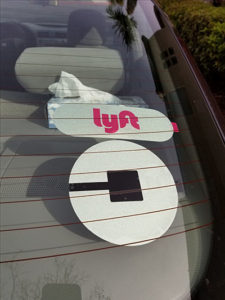 Uber and Lyft stickers on the window of a ride-share car