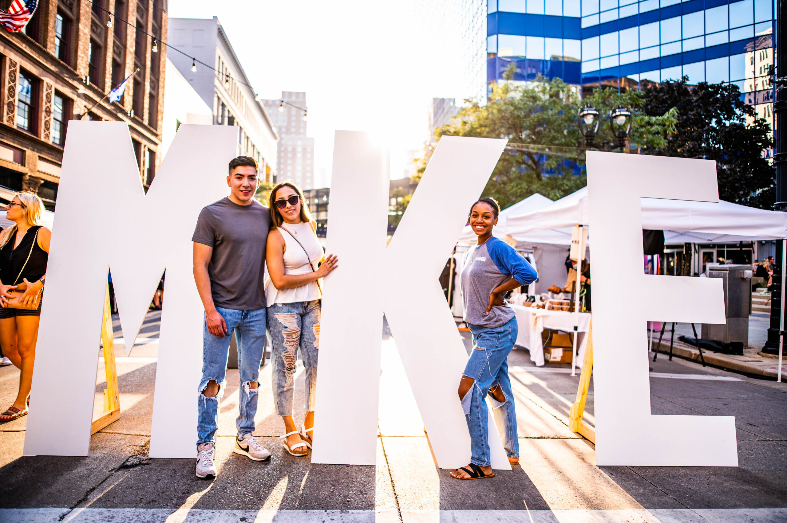Three young adults posing in Milwaukee's Deer District with three large letters M K E.