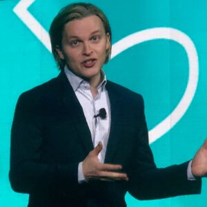 Ronan Farrow speaking at PCMA in front of a teal backdrop