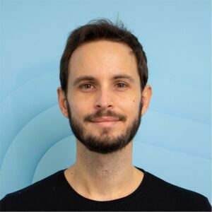 A portrait of Gilles Bertaux, author of this article. He is a white man with black hair and a beard, with a black t shirt