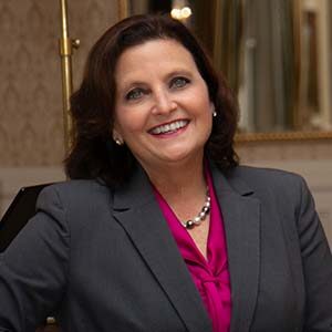 A portrait of Cheryl Twiss. She is a white woman with dark wavy hair and a grey suit jacket