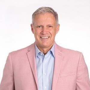 A portrait of David Curell. He is a white man with combed grey hair and a pink suit jacket