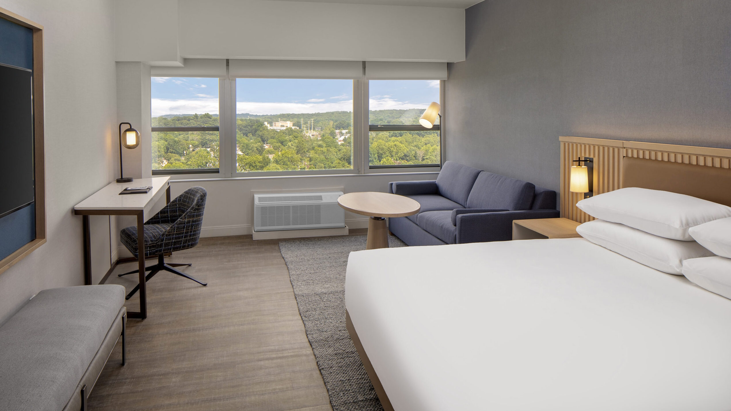 A guest room in Hyatt Regency Morristown with grey walls and furnishings, a desk and a view of a forest 