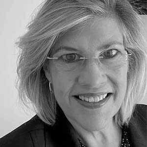 A black and white portrait of Julianne Juergens. She is an older white woman with short white hair and a black suit jacket