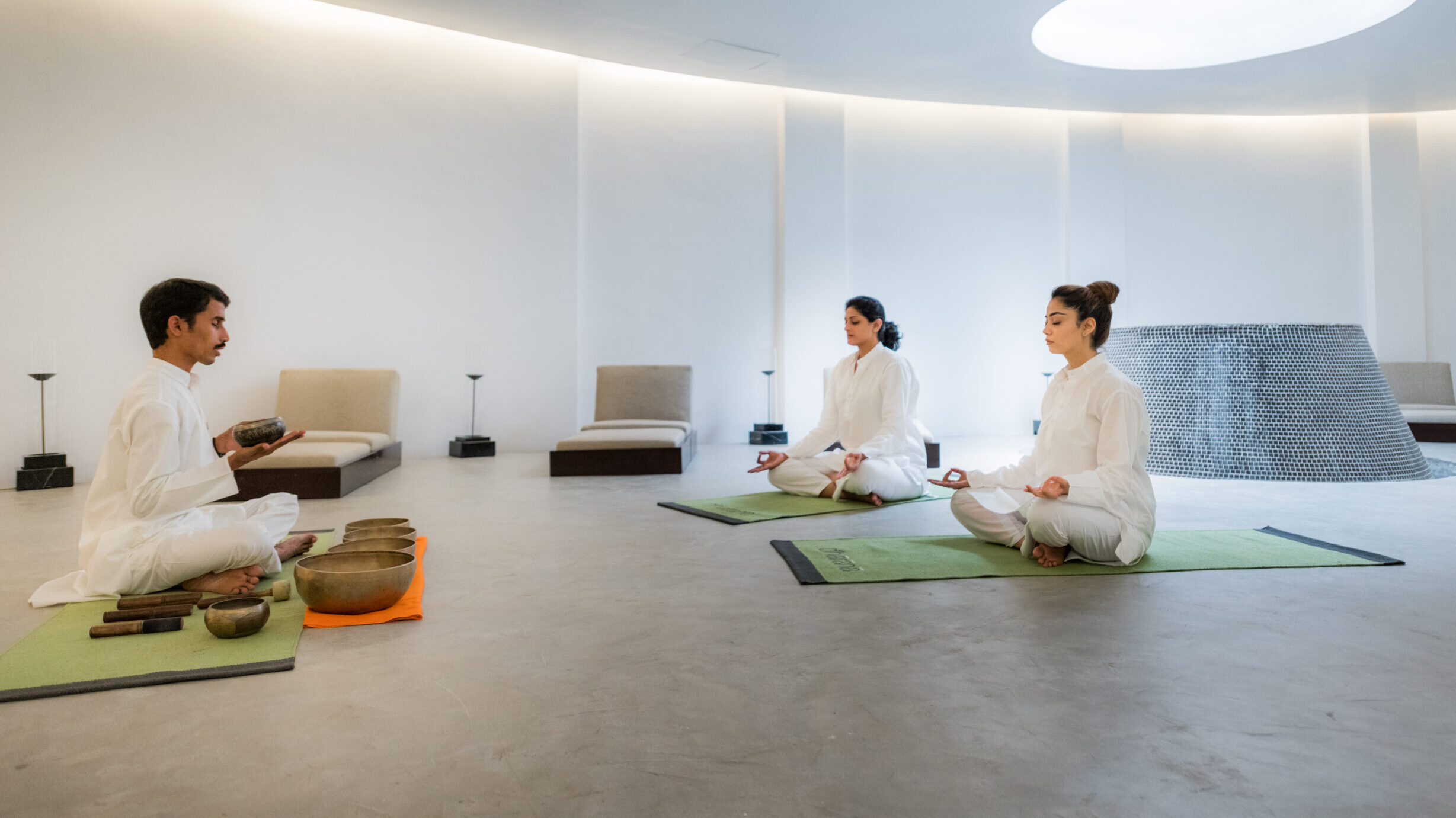 A small group of people meditate together on green mats in a white room at Hilton Shillim Estate Retreat & Spa