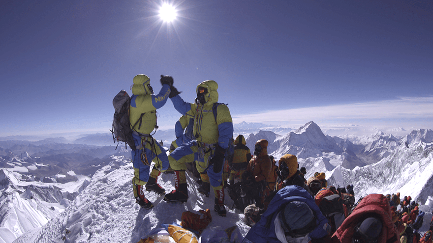 A group of climbers reaching the summit of Mount Everest. Two are holding hands