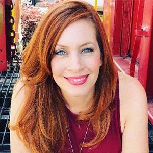 A portrait of Erynn Torrenga. She is a white woman with wavy red hair and a magenta blouse