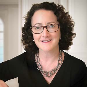 A portrait of Jennifer C. Squeglia. She is a white woman with curly black hair, square glasses and a black blouse