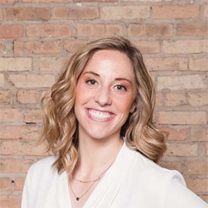 A portrait of Julie Knowles. She is a white woman with blonde wavy hair and a white blouse