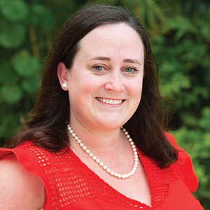 A portrait of Kelly Gallagher. She is a white woman with dark straight hair and a red blouse