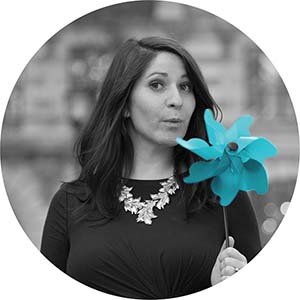 A black and white portrait of Lizz Torgovnick. She is a white woman with long dark hair holding a bright blue pinwheel