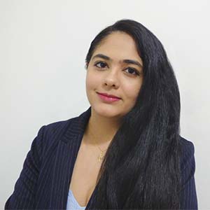 A portrait of Sonali Nair. She is a South Asian woman with long black hair and a striped suit jacket