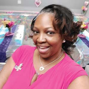 A portrait of Stephanie A. Watson. She is a black woman with short wavy hair and a pink blouse. She is posing in front of decorated tables