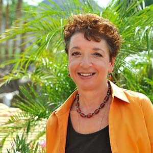 A portrait of Teri Agosta. She is a white woman with short curly brown hair and a yellow jacket