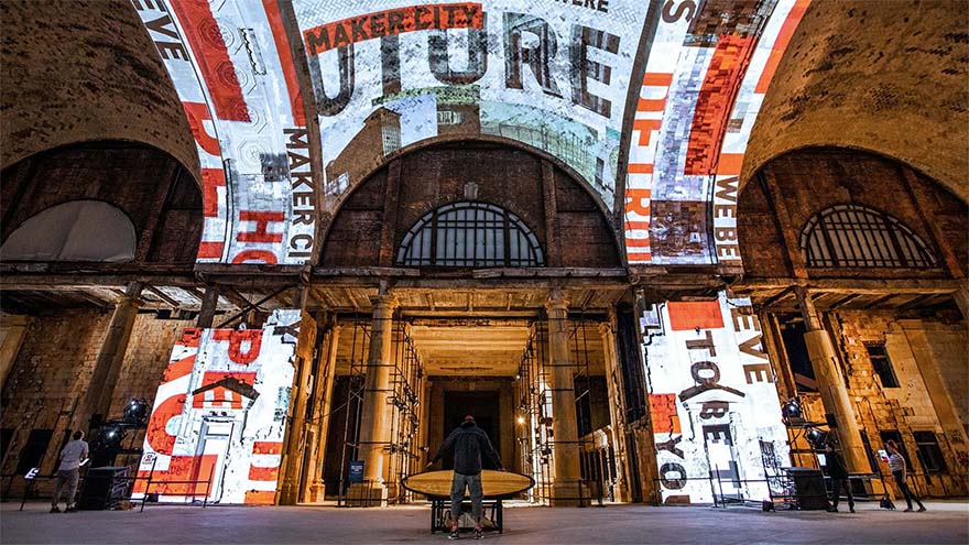 The interior of an abandoned building in Detroit with black, white and red patterns projected onto the ceiling and wall. Text reads "Maker city, future, hope, to be"