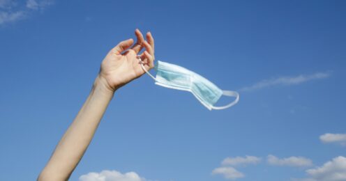 A person holding up a surgical mask with one hand