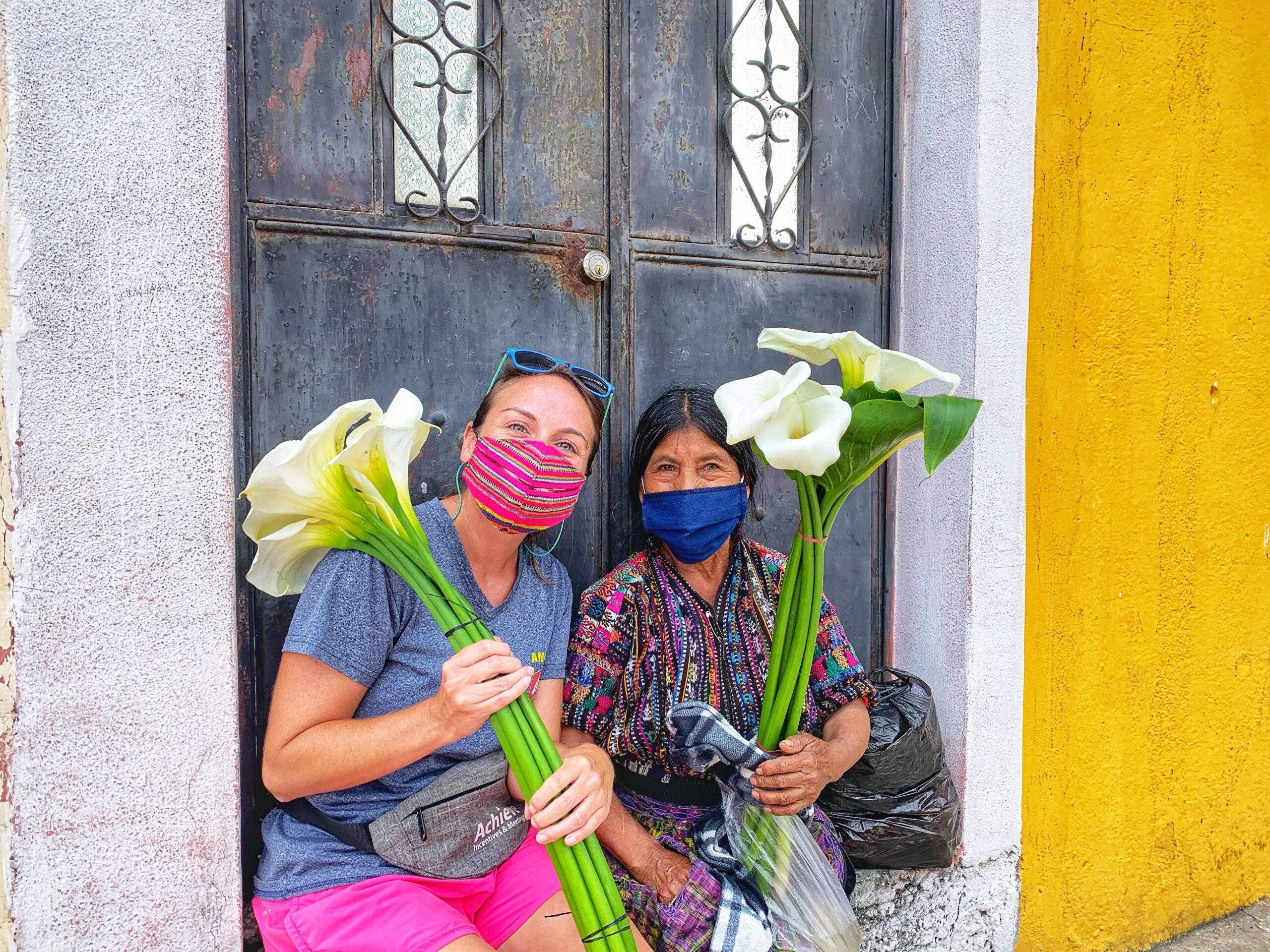 Ashley Lawson posing with a Guatemalan woman on a doorstep. They are both holding large Cala lillies