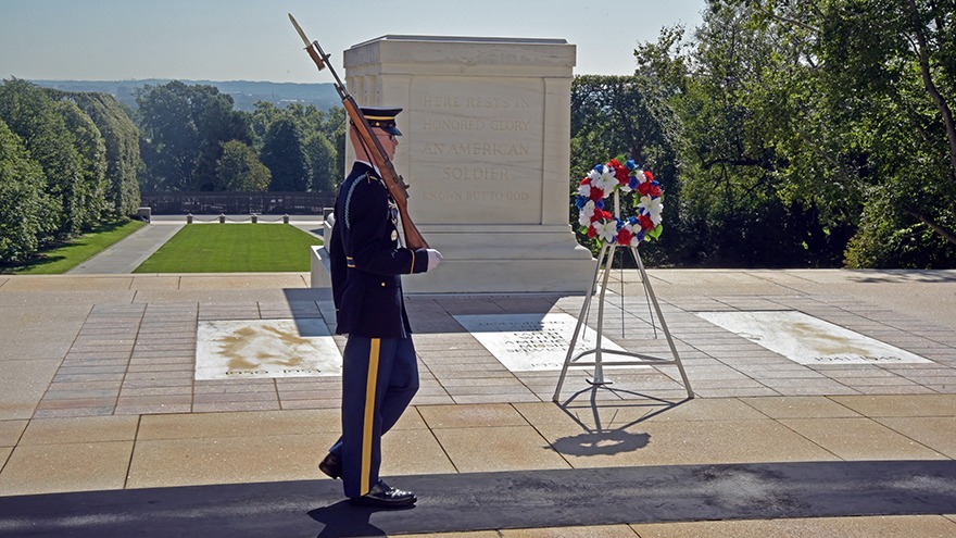 A marine holding a bayonet marches in front of a soldier's grave in Arlington