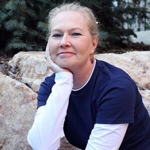 A portrait of Michelle Bruno. She is a blonde white woman with a dark t shirt over a long sleeved white shirt