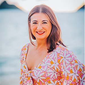 A portrait of Fabiola Sotomayor. She is a brown woman with wavy brown hair and a pink floral blouse