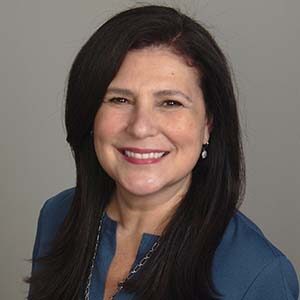 A portrait of Flávia Light. She is a brown woman with long black hair and a blue blouse