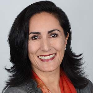 A portrait of Leonie Patrick. She is a white woman with wavy black hair, a grey blouse and a red scarf