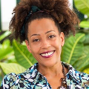 A portrait of Lily Carr. She is a black woman with an afro tied in a ponytail and a blue floral blouse