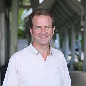 A portrait of Nigel Fisher. He is an older white man with dark combed hair and a white polo