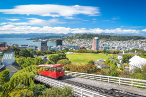 A red cable car on a track with a city in the background in New Zealand