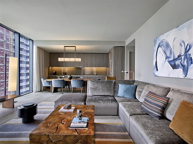 The sitting area and kitchen of a room in East Hotel Miami. The walls, floors and couch are grey with orange and blue accents