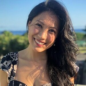 A portrait of Miju Kim. She is an Asian woman with wavy black hair and a black floral blouse.