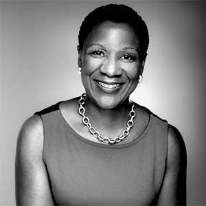 A black and white portrait of Michelle Mason. She is a black woman with short natural hair, a thick chain necklace and a blouse