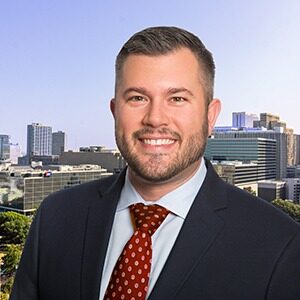 A portrait of Anthony Molino. He is a white man with a short beard with a black suit and a red tie.