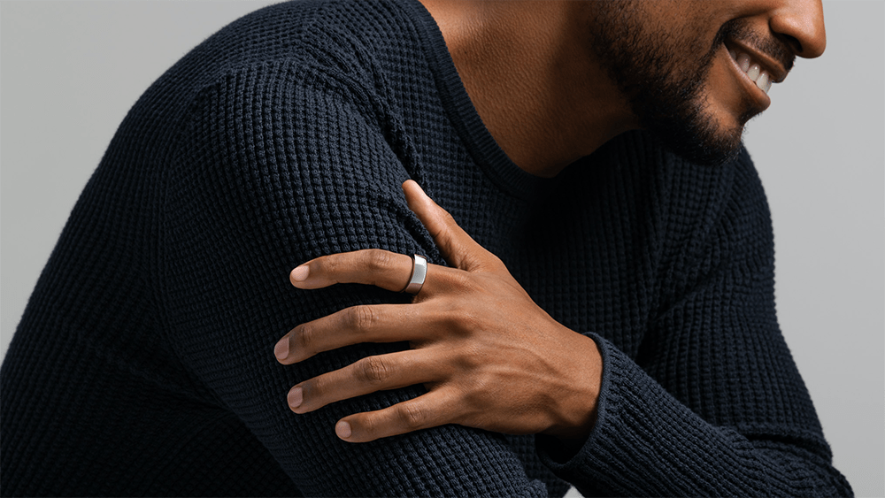 A black man wearing a black shirt has an Oura ring on, a solid silver-colored ring