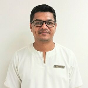 A portrait of Subhash Shanbhag. He is a Thai man with a white work shirt and square glasses.