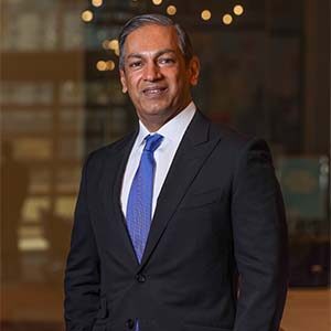 A portrait of meetings professional Sherrif Karamat. He is a brown man with a black suit and blue tie