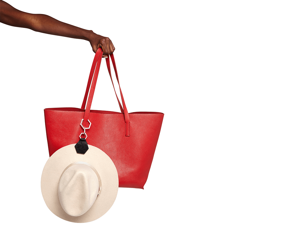 A wide red laptop-sized purse with an hexagonal hat clip holding a blush pink hat.