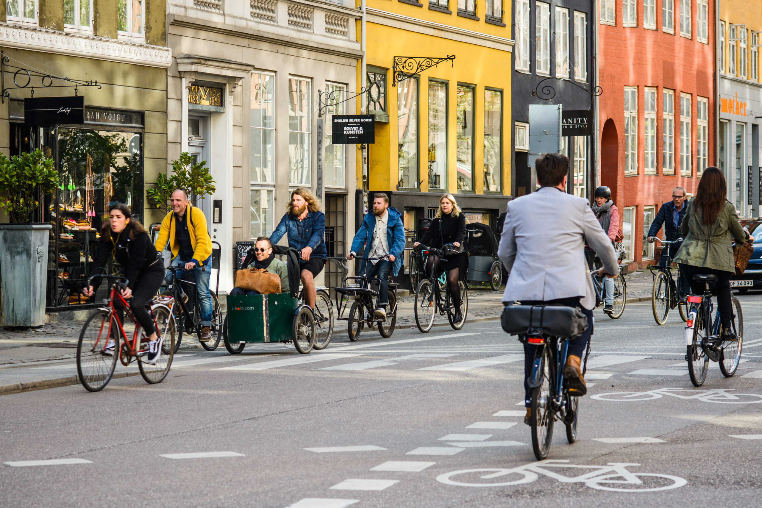 A street in Copenhagen. People ride bicycles on the street in front of colorful rowhouses.