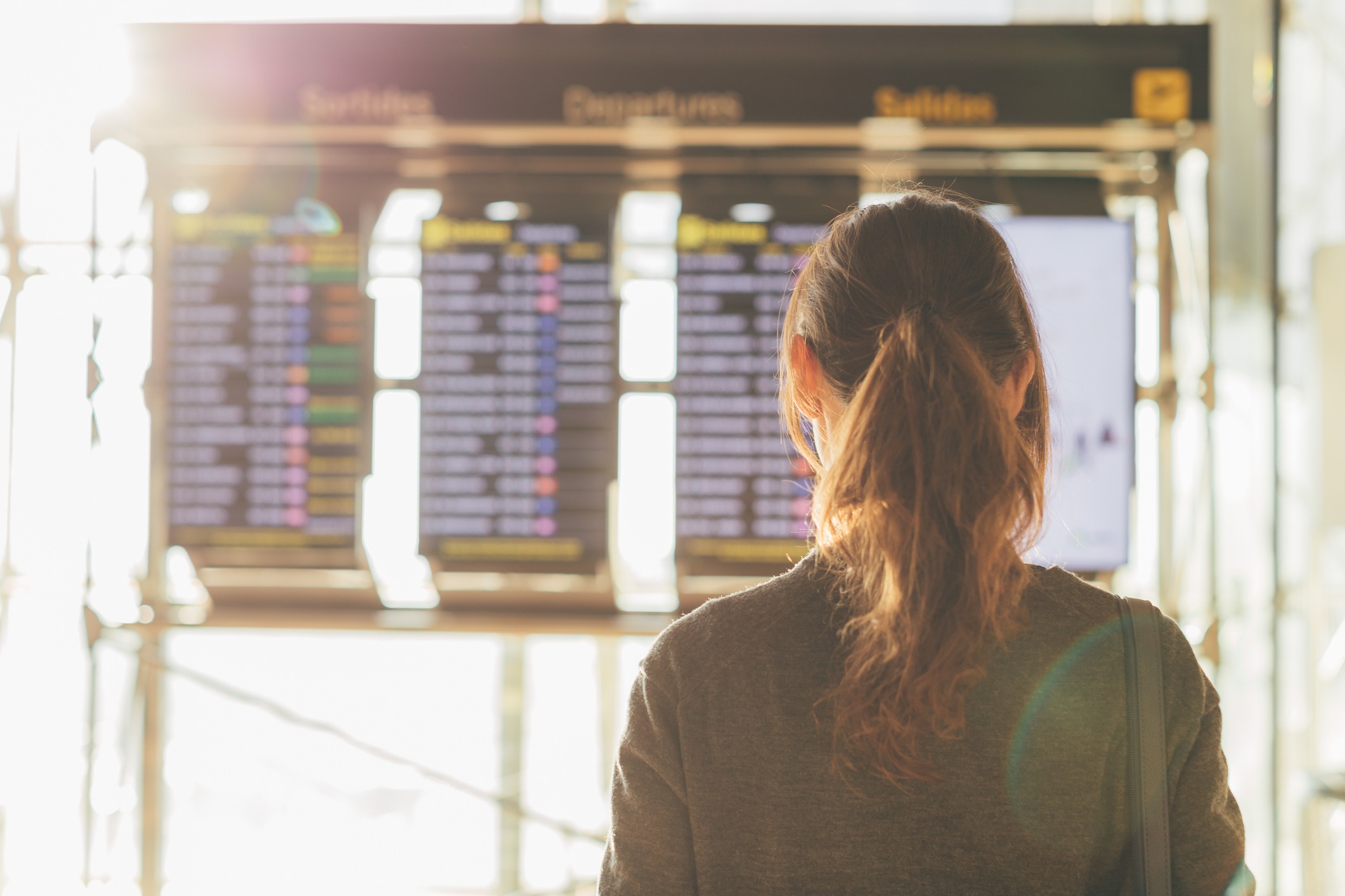 A woman with brown hair looks at a board of flight departures and arrivals.