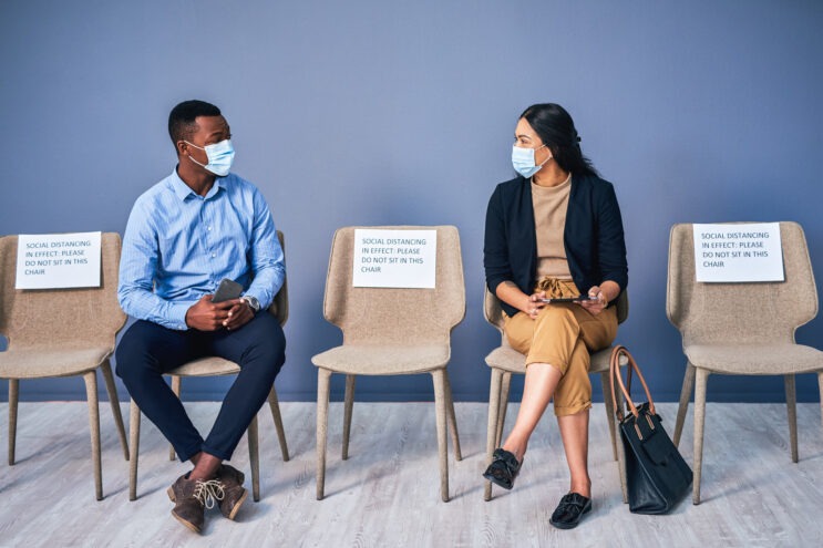 Two people wearing masks sitting next to each other.