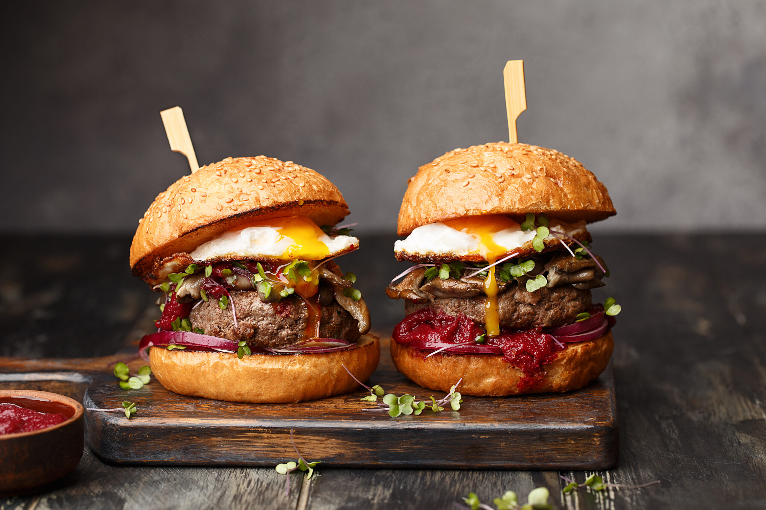Two hamburgers with fried eggs, sprouts, red onions, mushrooms and sauce