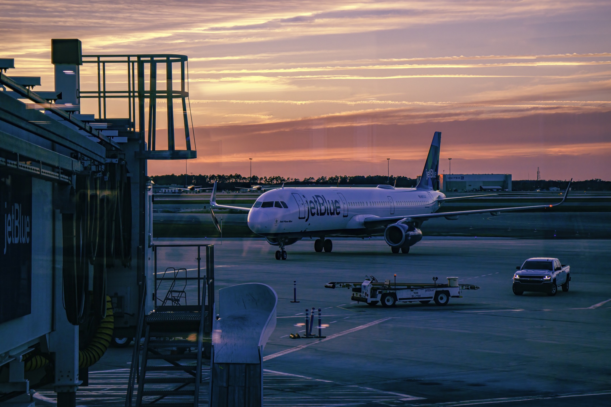 A jetBlue plane on the runway at sunset.
