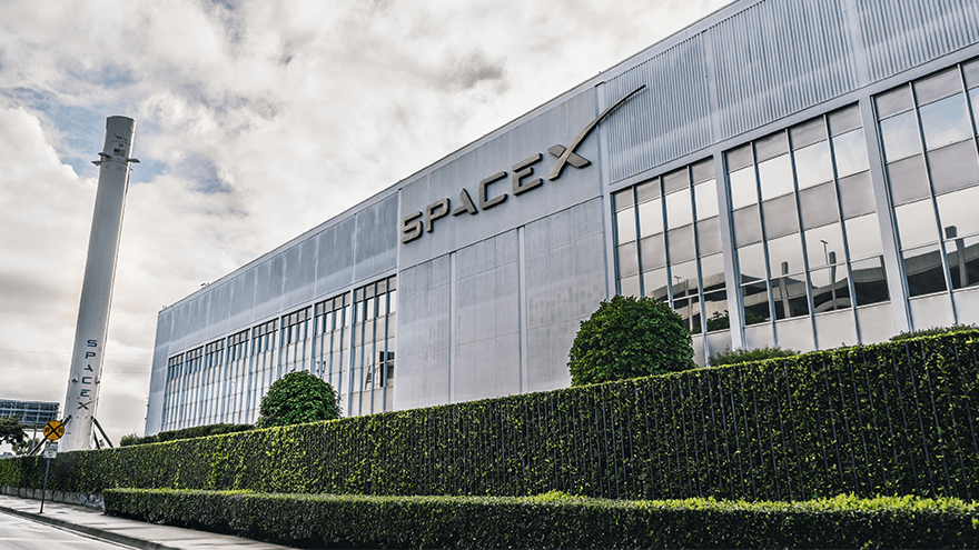 The front of SpaceX headquarters. It is a gray warehouse with a small hedge