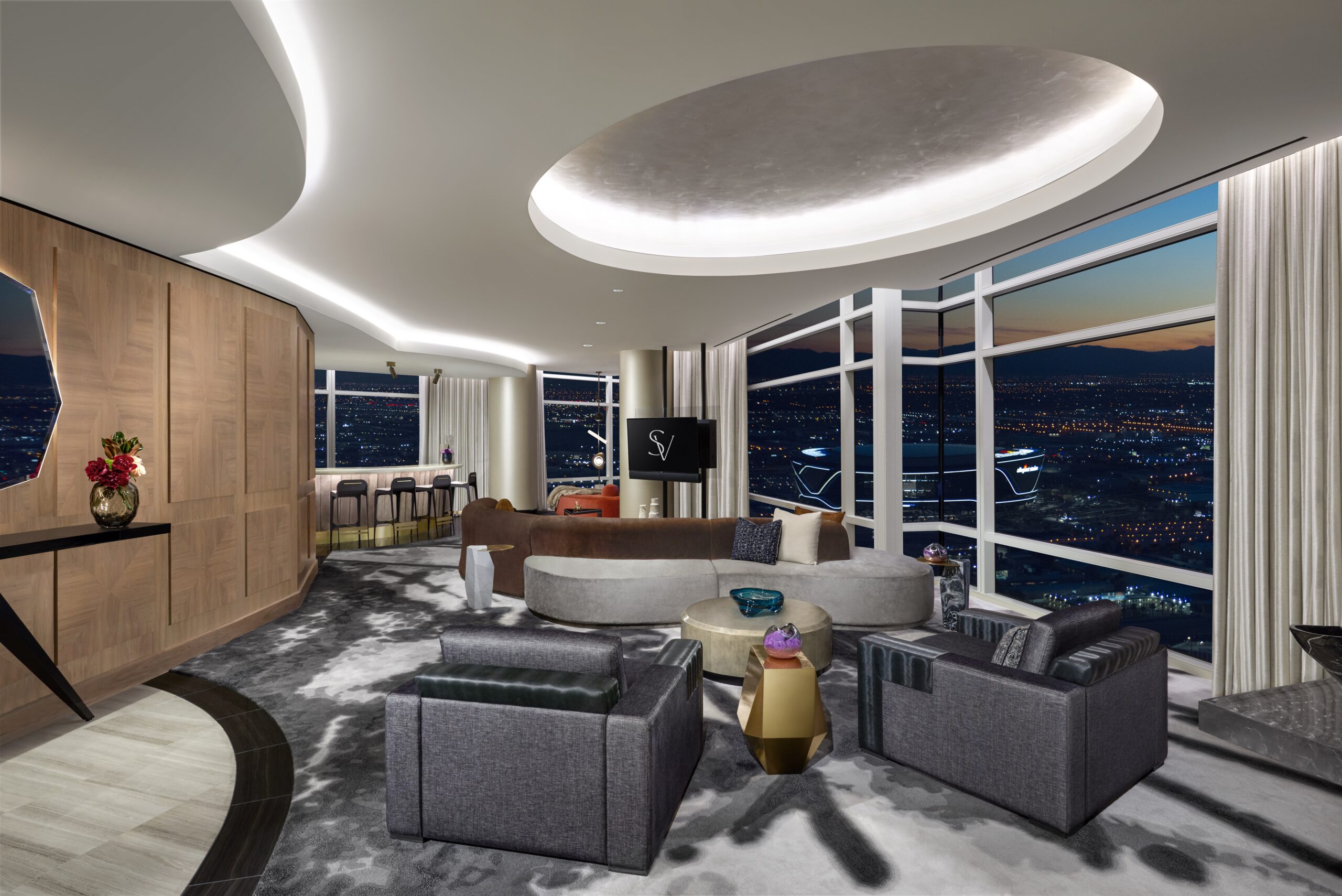 Rendering of the living room in Skyvilla at ARIA Resort & Casino. Its gaming and meeting options are extensive. The room has floor-to-ceiling windows, grey armchairs and patterned carpet.