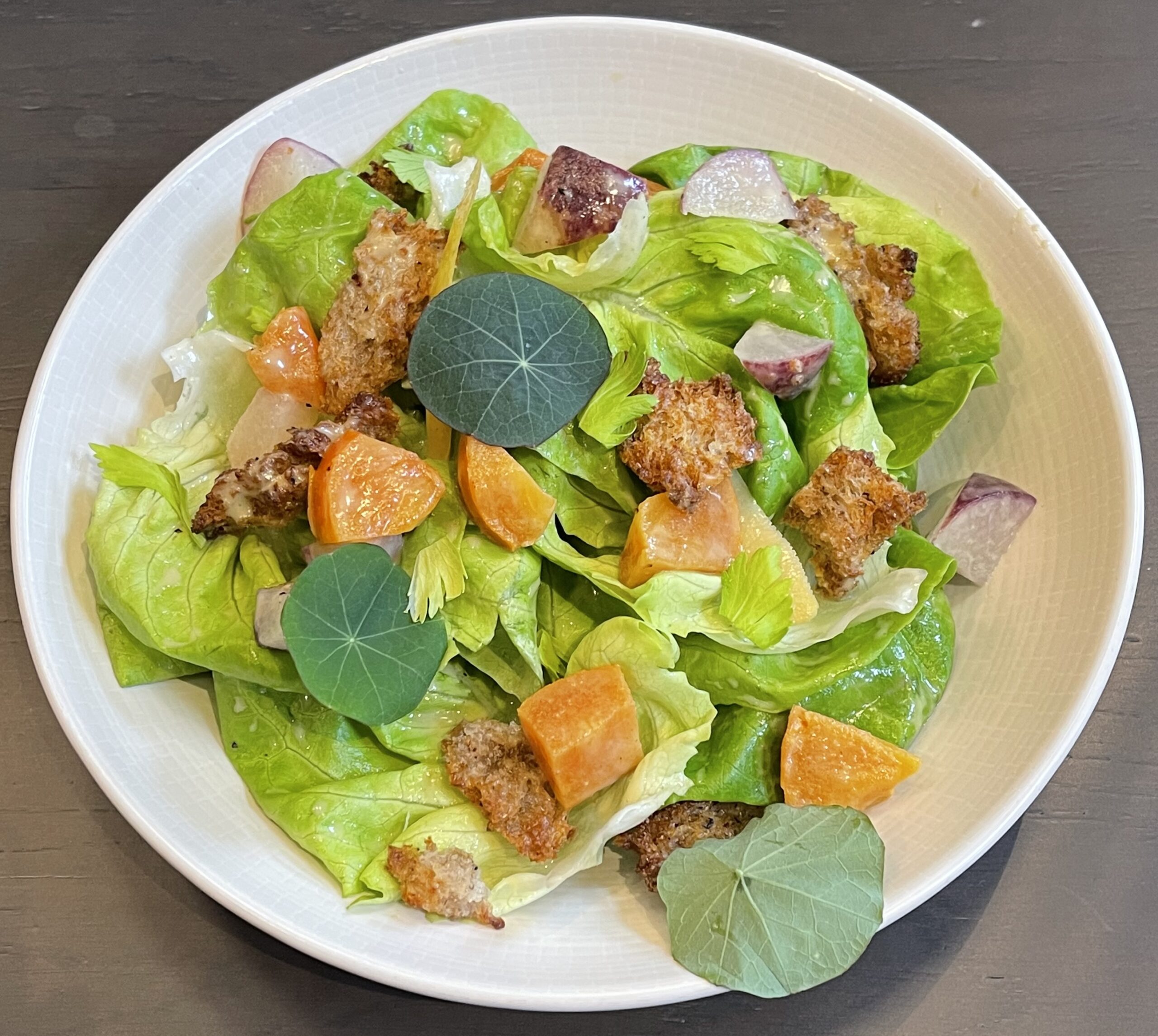 A plate of salad with various types of lettuce, chicken and croutons. 