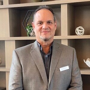 A portrait of German Villa, the new director of sales and marketing at Hilton Aventura Miami. He is a balding man with a short beard and grey suit.